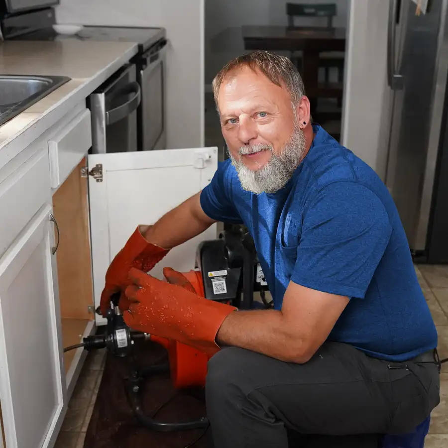 Plumber with plumbing tools kneeling fixing a sink