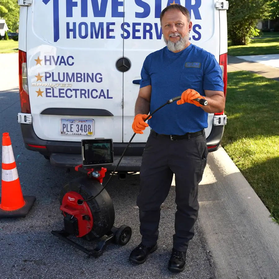 Plumber holding plumbing video camera inspection equipment standing in front of a Five Star Home Services Van