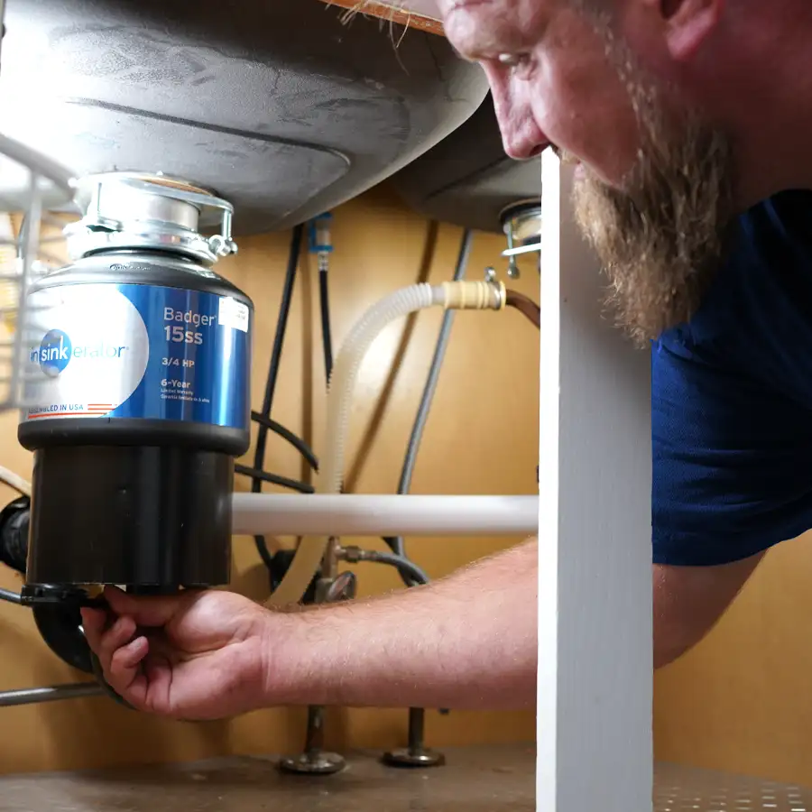 Plumber under a sink fixing a garbage disposal